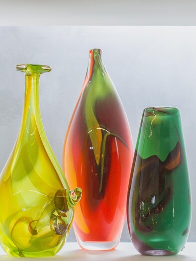 Drei kunstvolle Glasvasen in verschiedenen Farben stehen in einem hellen Hintergrund. Die Vasen sind in Gelb, Rot und Grün gehalten und zeigen interessante Formen. | © Atelier Faßwald - Michael Körbler