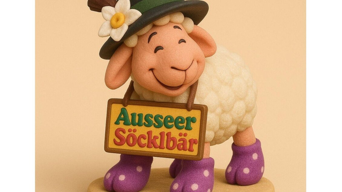 Ein fröhliches Schaf mit einem Hut und lila Socken hält ein Schild mit der Aufschrift "Ausseer Söcklbär". Es steht auf einem hellen Grund und lächelt. | © Ausseer Söcklbär_Barbara Prentner