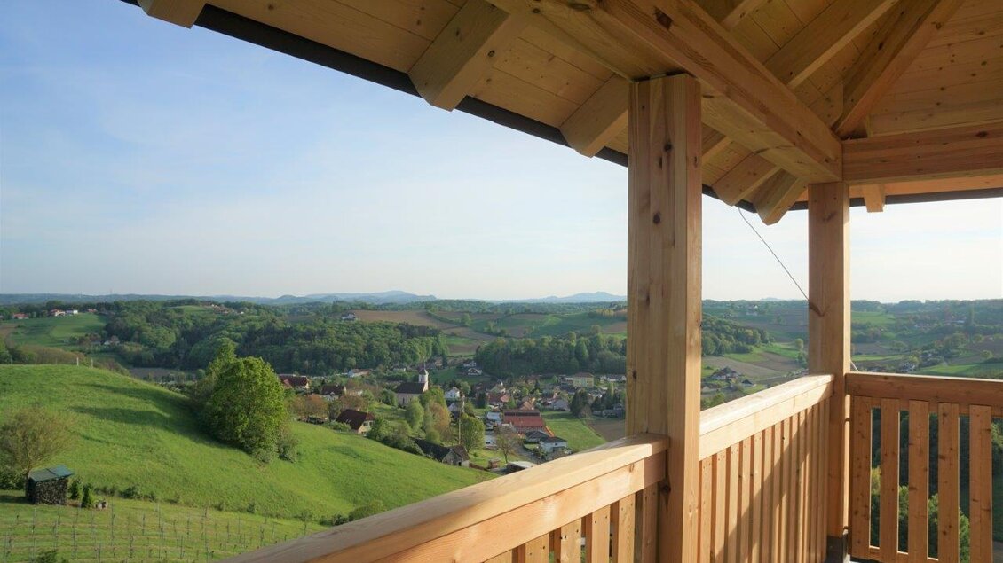 Eine Aussichtsplattform mit Sicht auf grüne Hügel und ein Dorf in der Ferne. Der Himmel ist klar und die Natur wirkt friedlich und einladend. | © Gemeinde Unterlamm