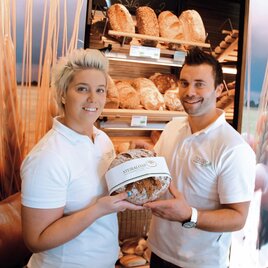 A friendly team presents fresh bread in a bakery. In the background, various types of bread can be seen. | © Bäckerei Masser