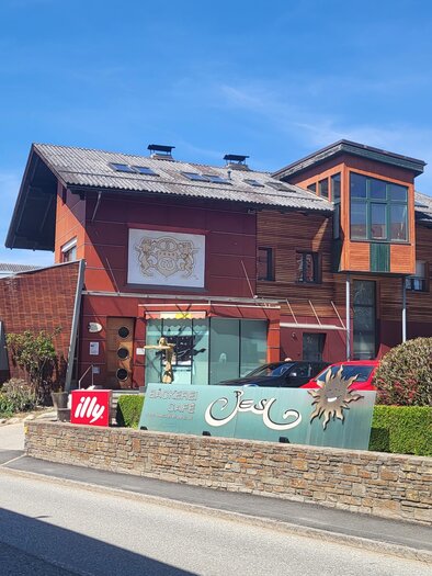 A modern two-story building with large windows and an inviting entrance area. In the foreground, decorative plants and a street sign are visible.