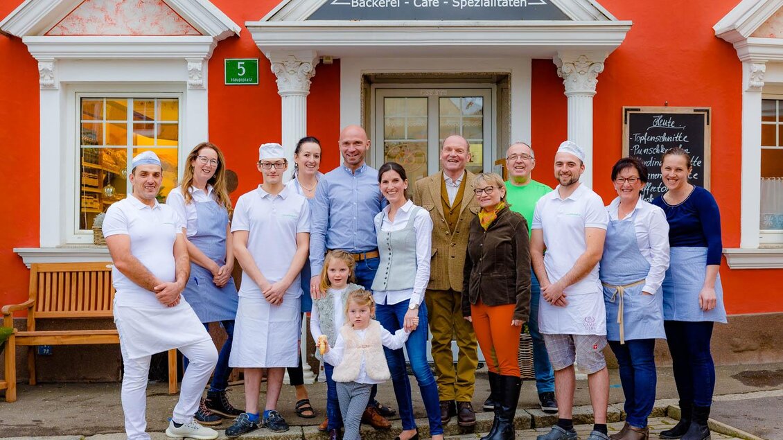 Eine Gruppe von Menschen steht vor einem bunter Gebäudefassade. Sie sind in Arbeitskleidung und präsentieren stolz ihr Café und ihre Bäckerei. | © Bäckerei Pirker