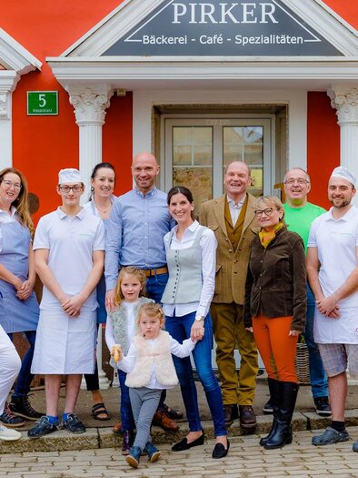 Eine Gruppe von Menschen steht vor einem bunter Gebäudefassade. Sie sind in Arbeitskleidung und präsentieren stolz ihr Café und ihre Bäckerei. | © Bäckerei Pirker
