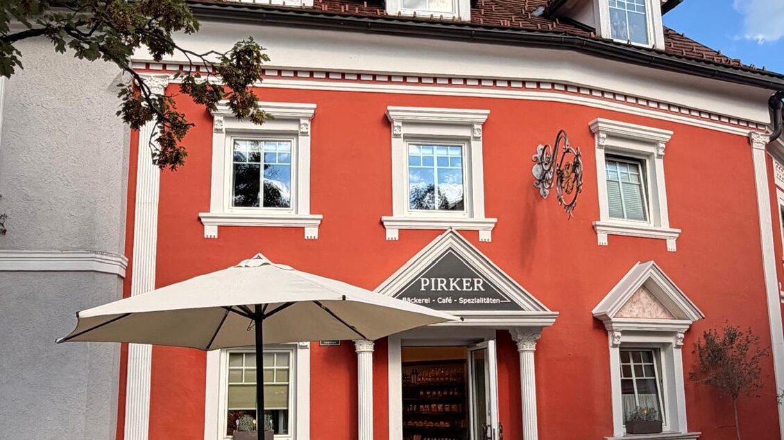 Ein gemütliches Café mit einer orangefarbenen Fassade und Tischen im Freien. Mehrere Personen genießen ihre Zeit im Außenbereich. | © Bäckerei Pirker