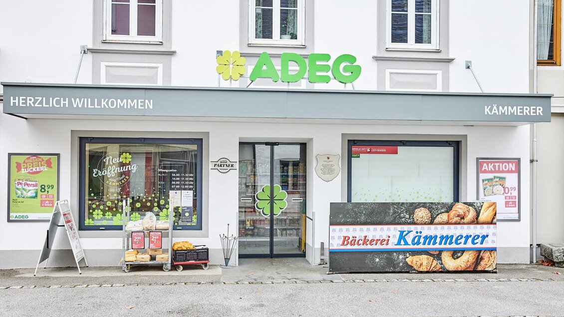 Ein Lebensmittelladen mit dem Namen "ADEG" und einer Bäckerei namens "Kämmerer". Die Fassade ist hell und einladend, mit Angeboten an der Außenseite. | © Thomas Sattler