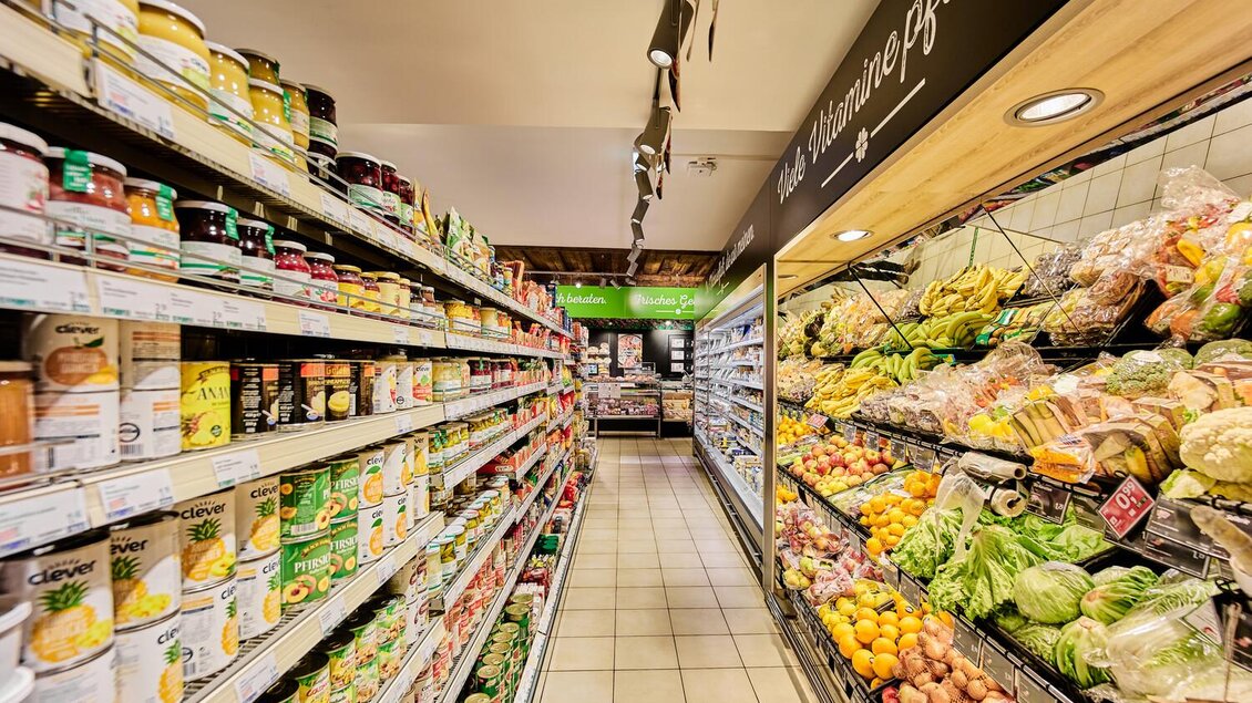 Ein bunter Supermarktgang mit Regalen voller Konservendosen und frischem Obst und Gemüse. Die Umgebung ist hell und einladend. | © Thomas Sattler