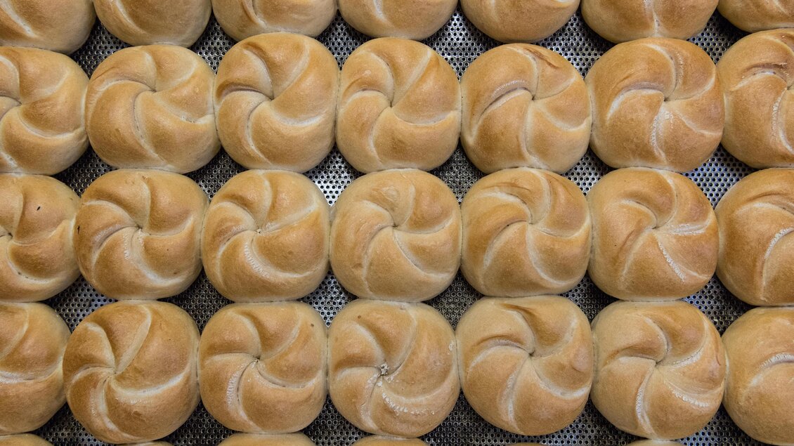 Eine Vielzahl von frisch gebackenen Brötchen in einem regelmäßigen Muster. Die Brötchen haben eine goldbraune Farbe und eine spiralförmige Oberlinie. | © Günter Ludwig Kämmerer