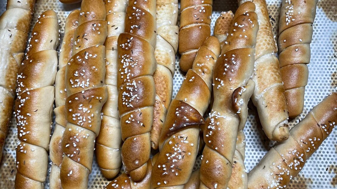 Eine Vielzahl von frisch gebackenen, goldbraunen Brotstangen liegt auf einem Blech. Die Brotstangen sind mit Sesam bestreut und wirken appetitlich. | © Bäckerei Steffl-Bäck