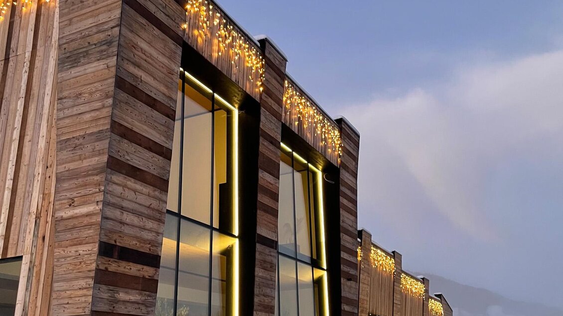 Ein modernes Gebäude aus Holz mit großen Fenstern. Die Fassade ist mit Lichtern geschmückt und es liegt Schnee auf dem Boden. | © Bäckerei Steffl-Bäck