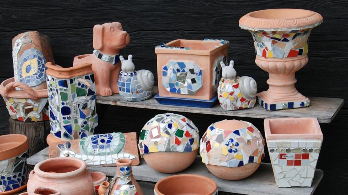 Bunte Töpferwaren und Dekorationsobjekte stehen auf einem Regal. Die Stücke sind mit Mosaiken verziert und zeigen verschiedene Formen und Farben. | © Bäuerliches Kunst- und Kleinhandwerk