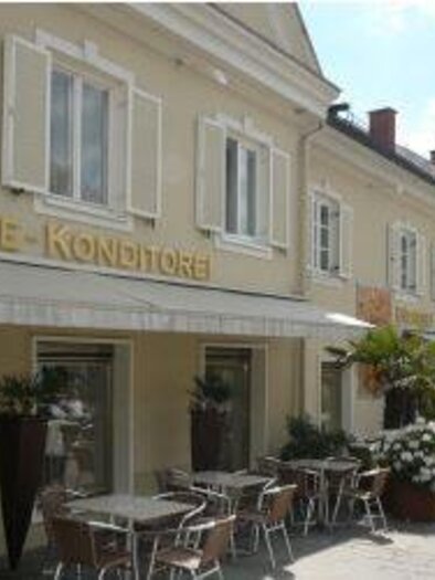 A charming café with an outdoor area and blooming plants. The buildings are painted in bright colors and invite you to linger.