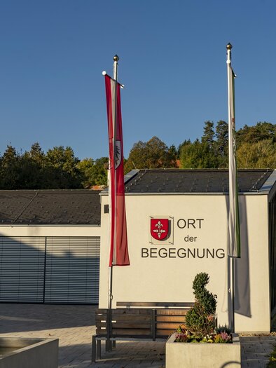 Ein modernes Gebäude mit der Beschriftung "Ort der Begegnung" ist im Vordergrund. Im Hintergrund steht eine kirchenartige Struktur mit einer auffälligen Kuppel. | © Kurkommission Bad Blumau