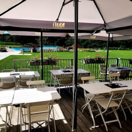 Eine Terrasse mit weißen Tischen und Stühlen unter Sonnenschirmen. Im Hintergrund ist ein gepflegter Garten mit einem Pool zu sehen. | © Stadtgemeinde Fehring