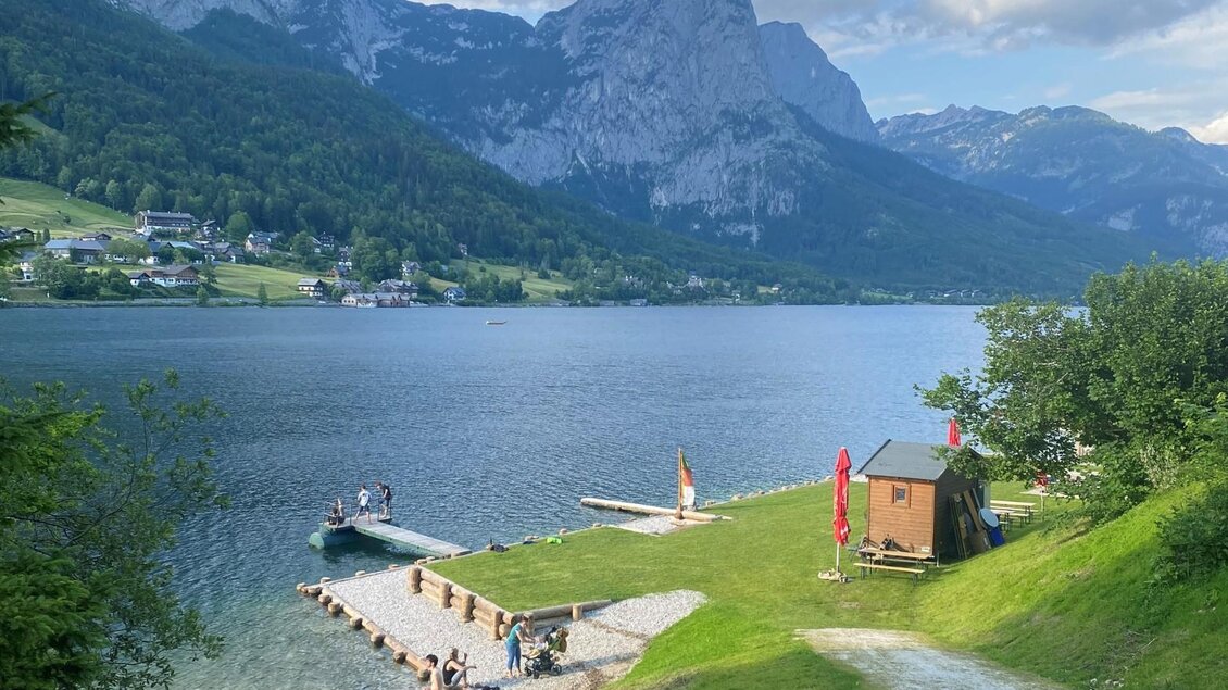 <p>Der malerische Grundlsee umgeben von der Berglandschaft des Ausseerlandes mit einem Seezugang aus Holz und Kies. Menschen genießen den Blick auf das steirische Meer.</p> | © Bettina Scheck
