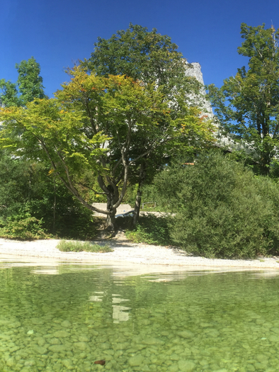 <p>Das Seeufer des klaren Grundlsees umgeben von grünen Bäumen und den Bergen des Ausseerlandes dahinter. Die Uferseite mit feinem Kies strahlt eine ruhige Atmosphäre aus.</p> | © Tourismusverband Ausseerland