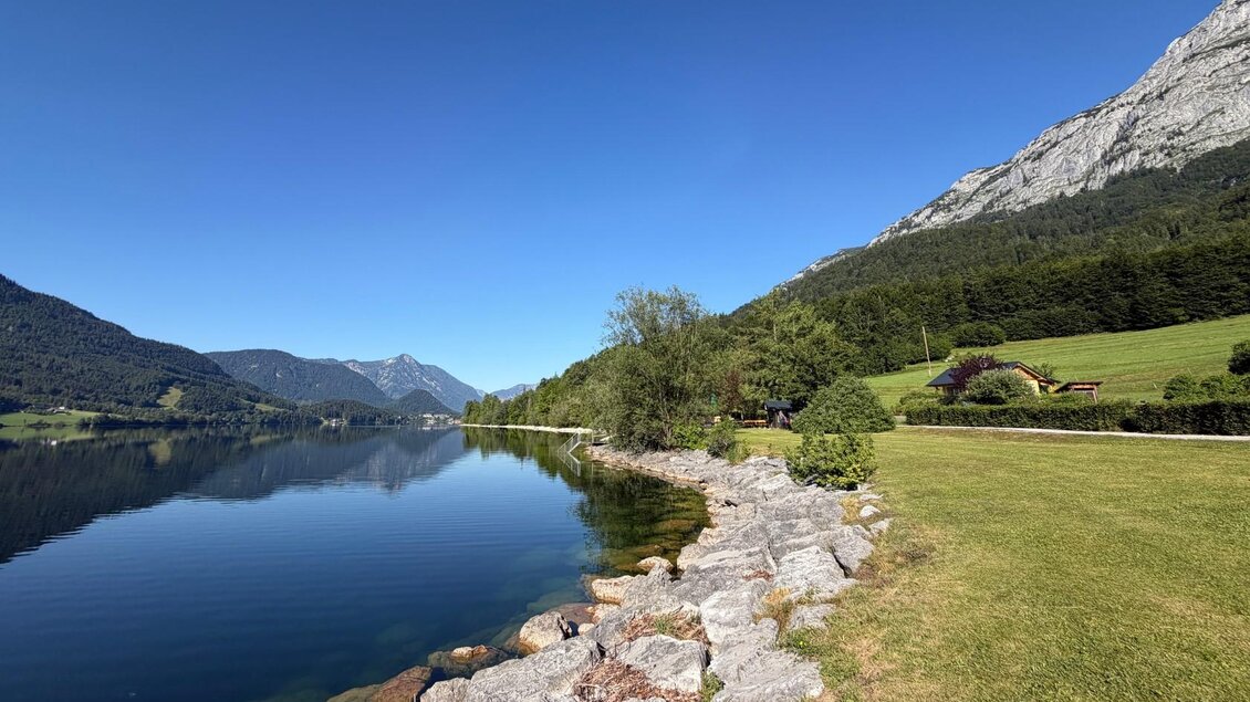 <p>Der ruhige Grundlsee umgeben von grünen Wiesen und den majestätischen Bergen des Ausseerlandes. Der Himmel ist klar und blau. Der Grundlsee kann über große Steine betreten werden.</p> | © Tourismusverband Ausseerland