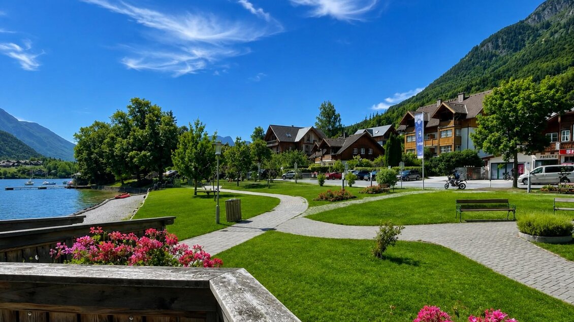 <p>Die traumhafte Berglandschaft mit dem Grundlsee und der grünen Parkanlage. Parkbänke im Gemeindepark und Häuser entlang der Straße sind im Hintergrund zu sehen.</p> | © Tourismusverband Ausseerland