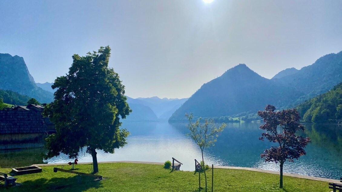 Der ruhige Grundlsee umgeben vom Toten Gebirge und saftigen Wäldern. Die Sonne scheint am Himmel und spiegelt sich traumhaft im Wasser. | © Tourismusverband Ausseerland