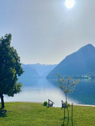 The tranquil Grundlsee surrounded by the Dead Mountains and lush forests. The sun is shining in the sky and reflects dreamily on the water. | © Tourismusverband Ausseerland