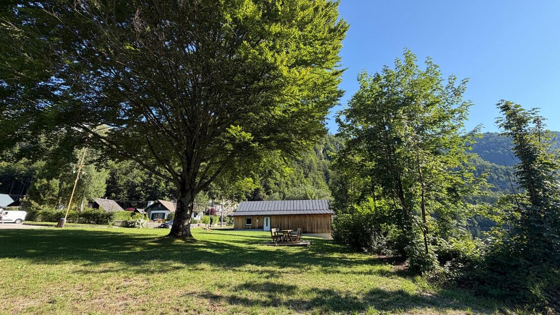 <p>Der ruhige Badeplatz Schachen-Siedlung mit großen Bäumen mietet ausreichend Schattenplätze an heißen Sommertagen. Im Hintergrund sind Häuser, eine Holzhütte und eine traumhafte Landschaft sichtbar.</p> | © Tourismusverband Ausseerland