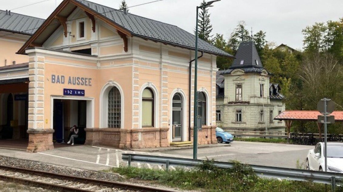 Der Bahnhof Bad Aussee mit seiner markanten Fassade und den historischen Gebäuden. Im Hintergrund sind Bäume und ein Parkplatz sichtbar. | © TVB Ausseerland Salzkammergut