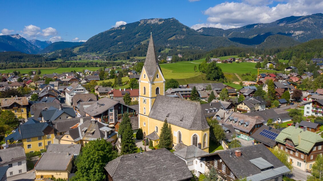 Ein malerisches Dorf mit einer auffälligen Kirche im Zentrum. Umgeben von grünen Bergen und traditionellen Häusern. | © TVB Ausseerland Salzkammergut/Karl Grieshofer