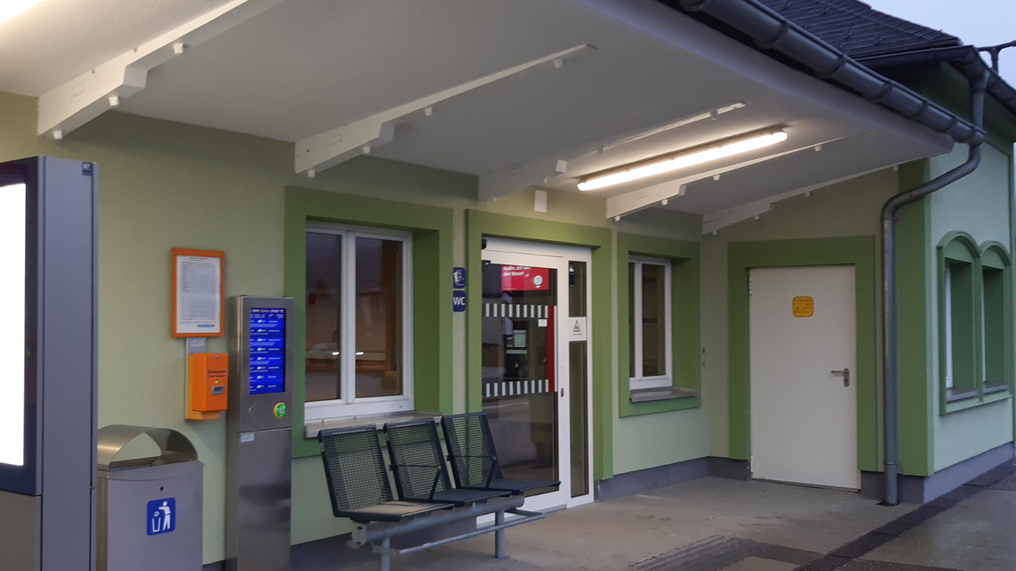 Ein Eingang zu einem Gebäude mit einem überdachten Bereich. Es sind eine Bank und verschiedene Informations- und Zahlungsmöglichkeiten sichtbar. | © TVB Ausseerland Salzkammergut_Daniela Casari