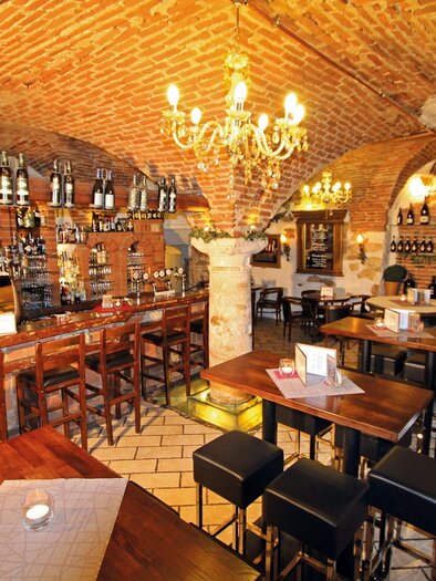Ein gemütliches Restaurant mit Ziegelsteinwänden und einer warmen Beleuchtung. Tische und Stühle laden zum Verweilen ein, während die Bar mit einer Auswahl an Flaschen bestückt ist. | © Bar Rathaus Vinarium