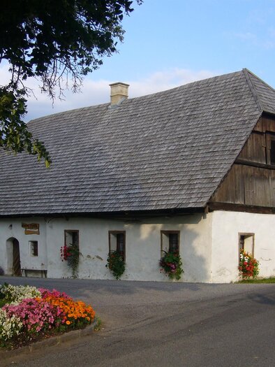 Ein traditionelles Bauernhaus mit einem steilen Dach und Holzverkleidung. Vor dem Haus wachsen bunte Blumen und es gibt eine ruhige Umgebung. | © Bauernmuseum Herkhof
