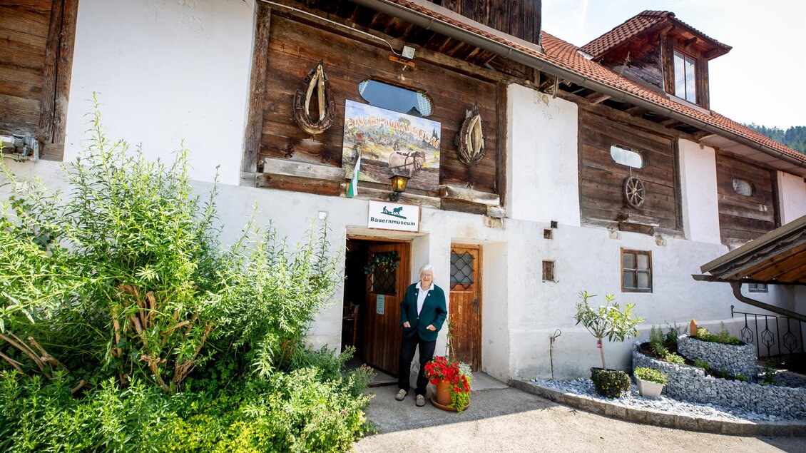 Ein historisches Gebäude mit einer ansprechenden Fassade aus Holz und Naturstein. Vor der Tür steht eine Person mit Blumen, umgeben von grünen Pflanzen. | © TVB Murau
