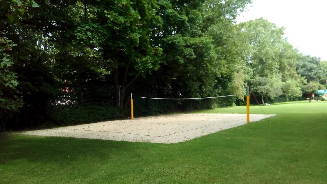 Ein Beachvolleyballfeld in einem grünen Park. Die Umgebung ist von Bäumen umgeben und das Feld ist mit Sand bedeckt. | © Gerlinde Kohl