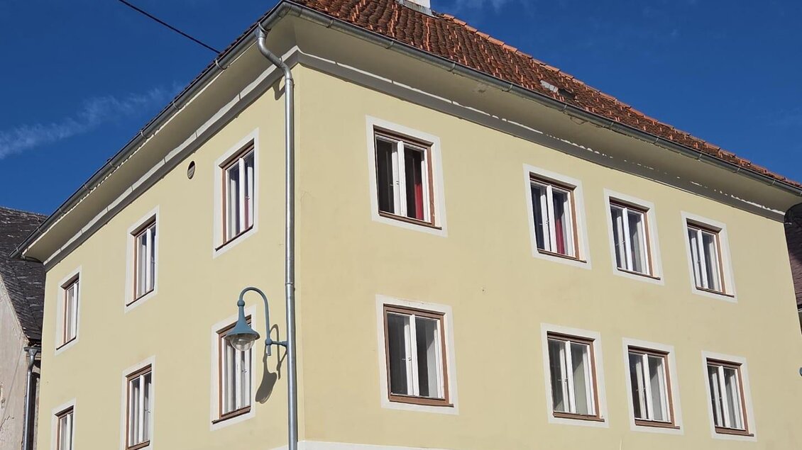 Ein gelbes Gebäude mit mehreren Fenstern und einem roten Dach. Es steht an einer Straßenecke unter klarem Himmel. | © Thomas Herzog