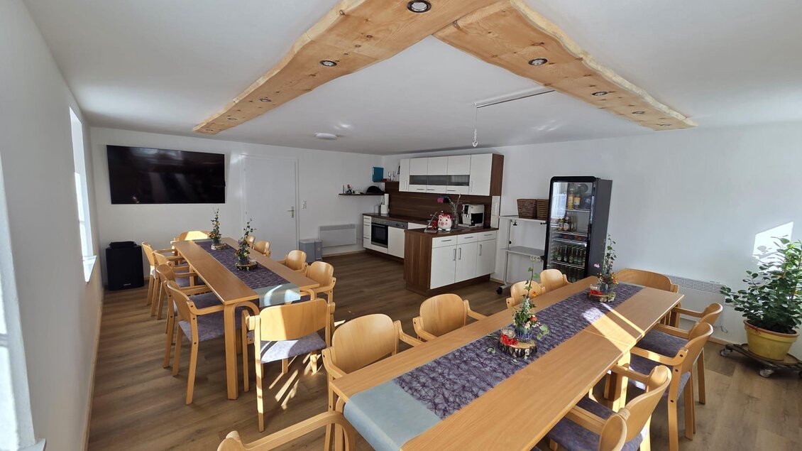 Ein moderner Essbereich mit Holzstühlen und einem langen Tisch. Die Küche ist gut ausgestattet und ein großer Fernseher hängt an der Wand. | © Thomas Herzog