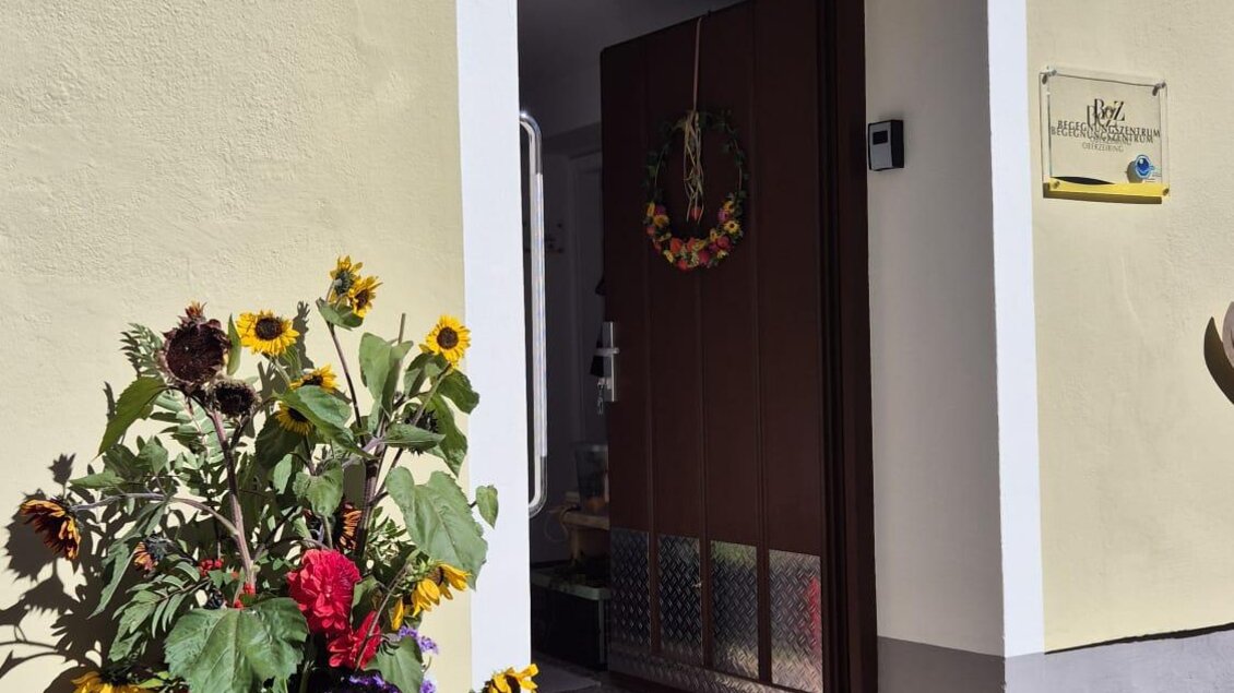 Eine einladende Haustür mit einem Blumenarrangement aus Sonnenblumen und bunten Pflanzen daneben. Der Eingang wirkt freundlich und einladend. | © Thomas Herzog