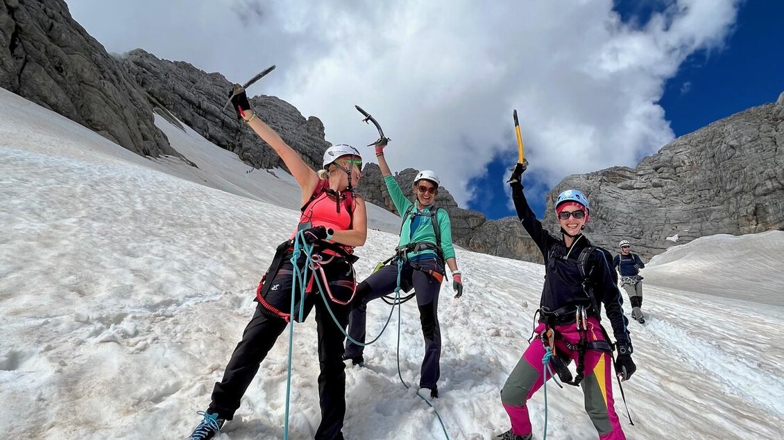 Drei Bergsteigerinnen stehen auf einem verschneiten Hang und feiern ihren Erfolg. Sie tragen Kletterausrüstung und zeigen mit ihren Eispickeln in die Luft. | © Hans Prugger