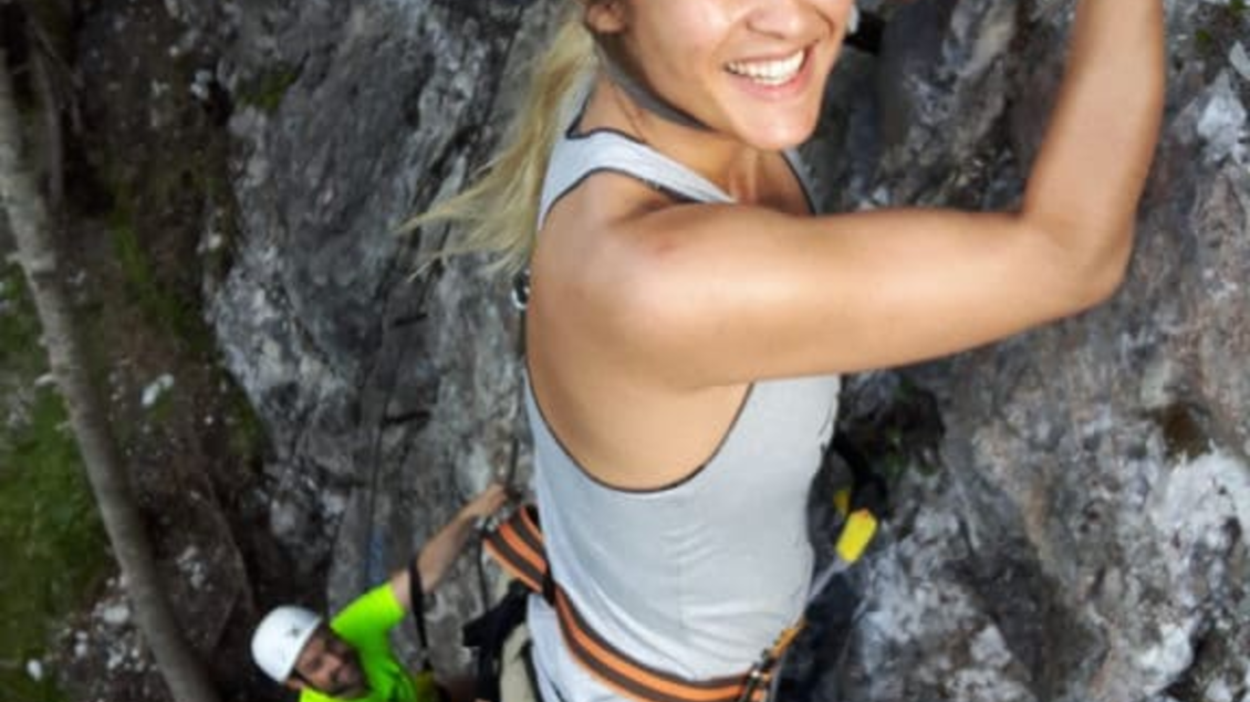 Eine Frau klettert an einer Felswand und lächelt dabei. Im Hintergrund ist eine andere Person, die ebenfalls klettert. | © Hans Prugger