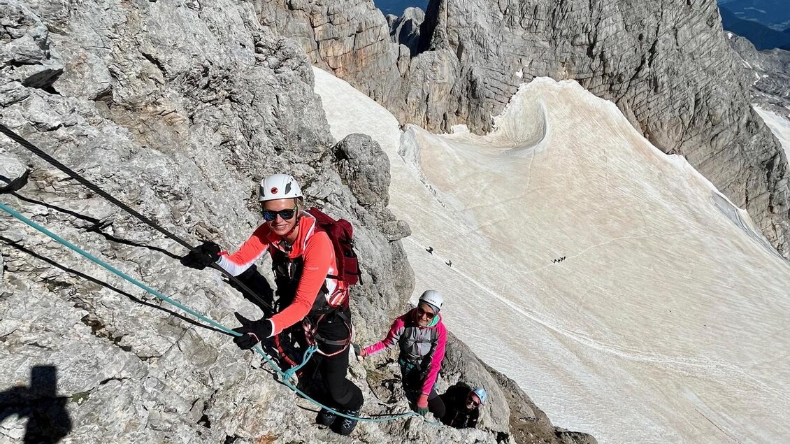 Zwei Kletterer steigen einen steilen Felsen hinauf. Im Hintergrund sieht man beeindruckende Berglandschaften und einen klaren blauen Himmel. | © Hans Prugger