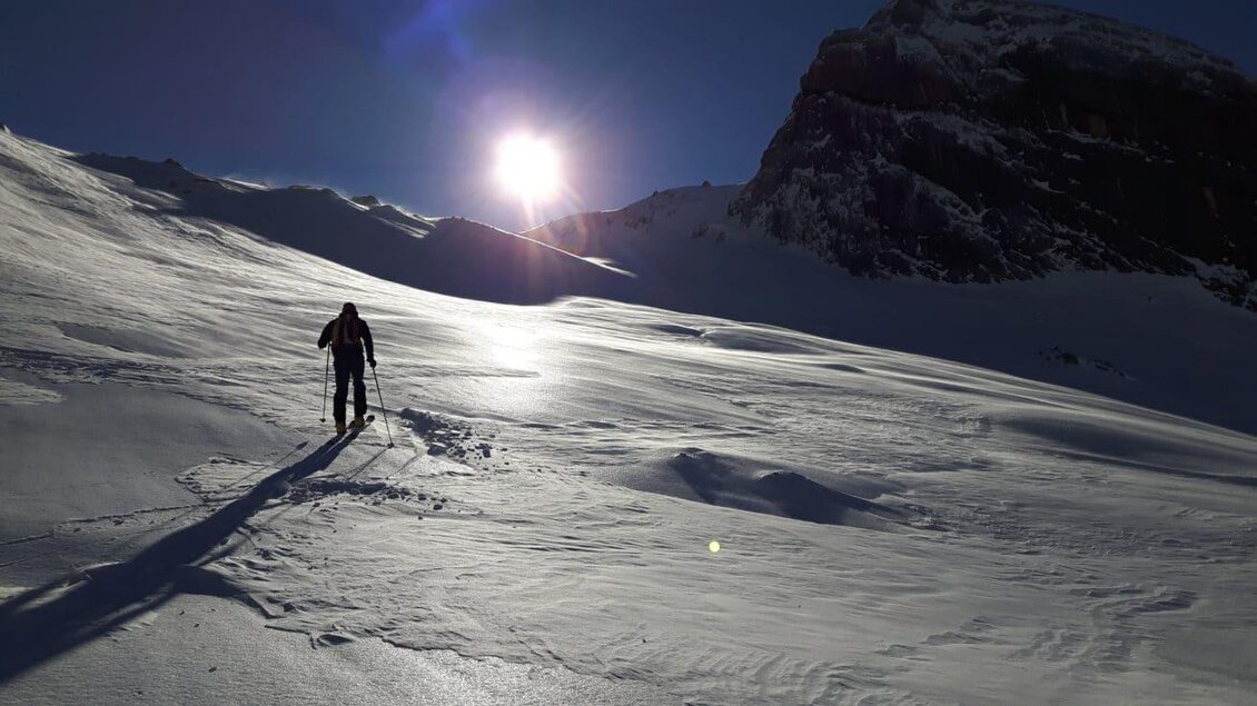 Ein Skifahrer wandert durch eine verschneite Landschaft. Die Sonne scheint hell über den Bergen. | © Hans Prugger