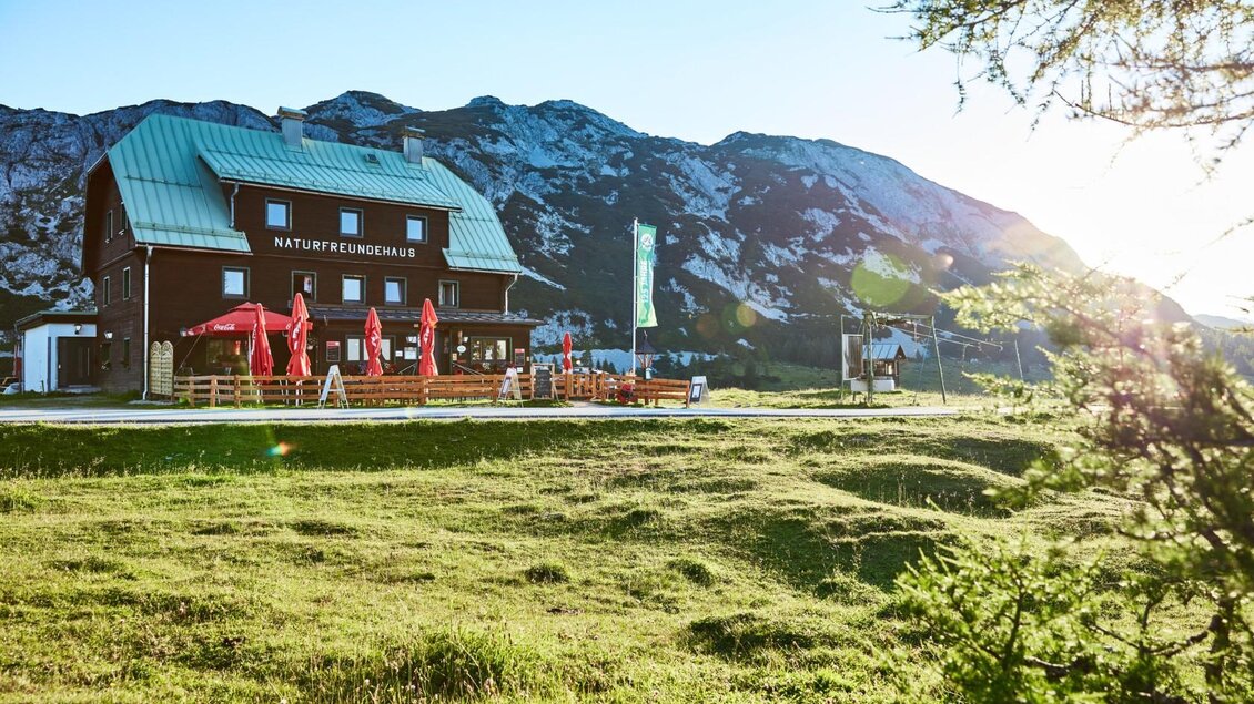 <p>Das sonnige Naturfreundehaus mit Terrasse und Sonnenschirmen. Im Hintergrund sind Berge zu sehen, und die Sonne strahlt warm über die Landschaft.</p> | © Karin Klammer Fotografie