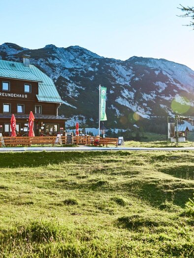 <p>Das sonnige Naturfreundehaus mit Terrasse und Sonnenschirmen. Im Hintergrund sind Berge zu sehen, und die Sonne strahlt warm über die Landschaft.</p> | © Karin Klammer Fotografie