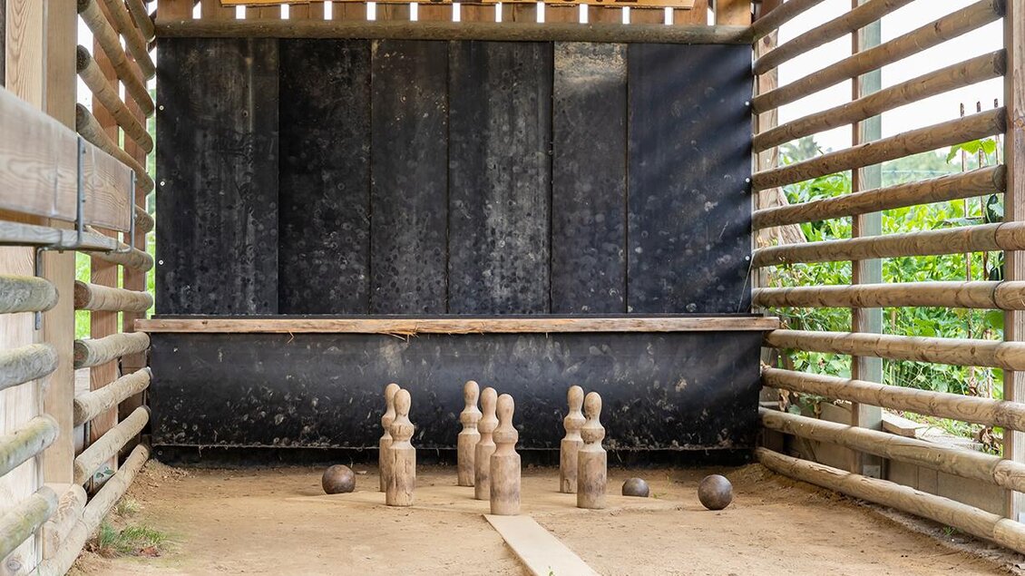 <p>Ein Holzspielplatz mit einem Spielbereich für Boule. Im Hintergrund sind Holzfiguren und ein Schild mit der Aufschrift "Gut Holz".Bergschenke Schlögl in Kirchberg an der Raab</p> | © Andreas Schlögl