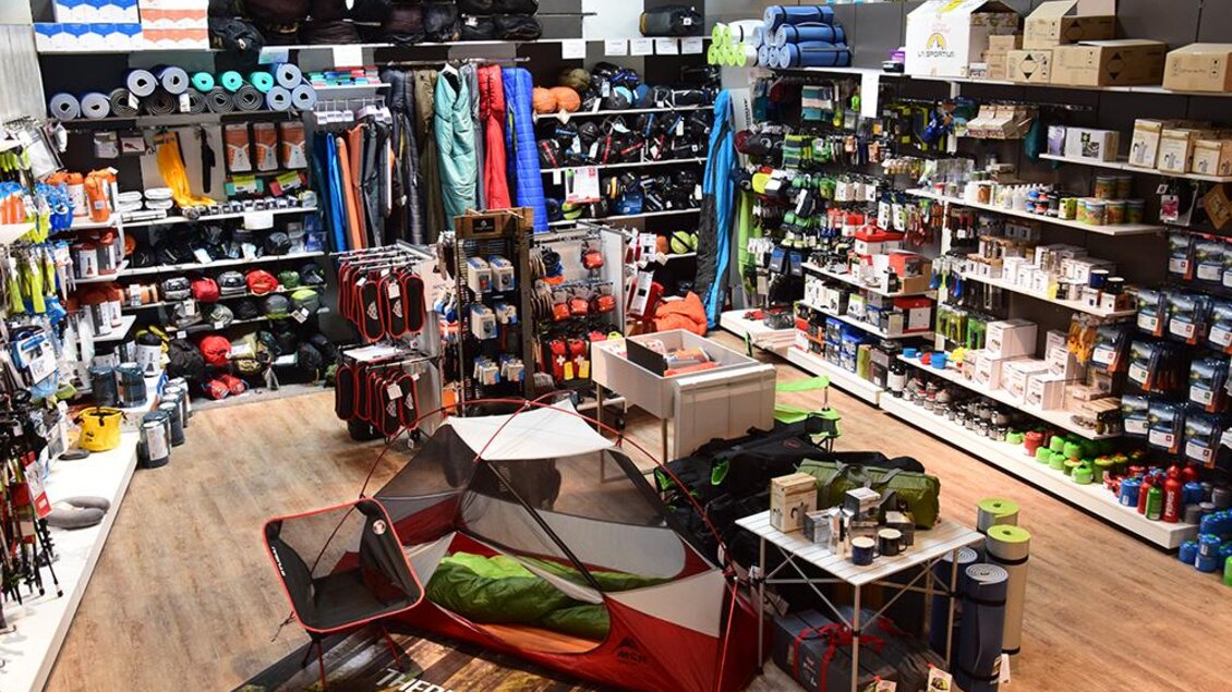 Ein gut ausgestatteter Outdoor-Laden mit Campingausrüstung und Zubehör. Zahlreiche Regale sind gefüllt mit Zelten, Schlafsäcken und anderen Freizeitartikeln.