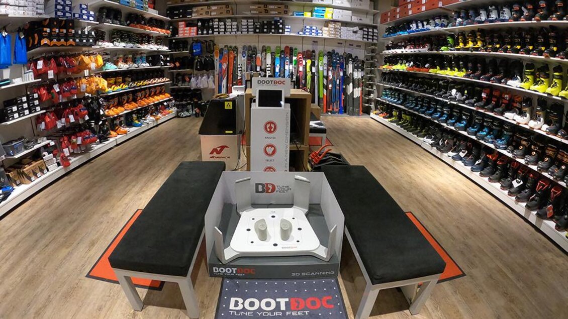 Ein Sportgeschäft mit Regalen voller Skischuhe und -ausrüstung. In der Mitte befinden sich Sitzplätze und ein Boot Doc Servicebereich.