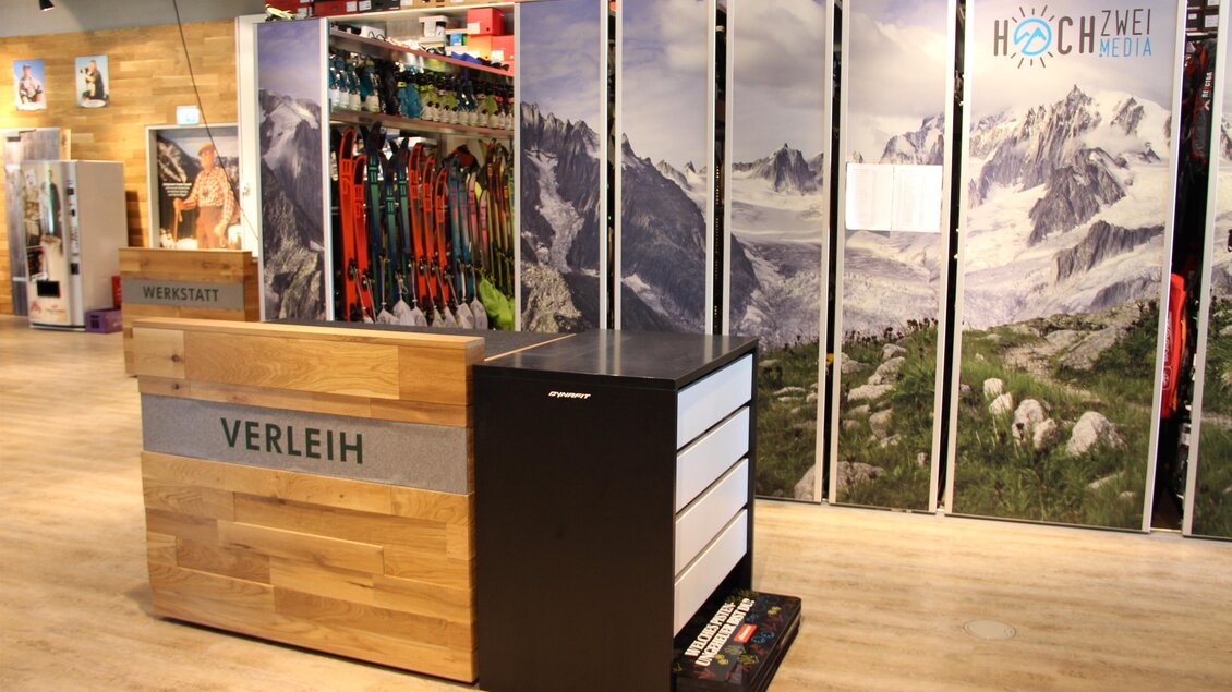 Ein Verleihbereich mit einem Holztheke und einem modernen Design. Im Hintergrund sind Bilder von Bergen und Natur zu sehen.