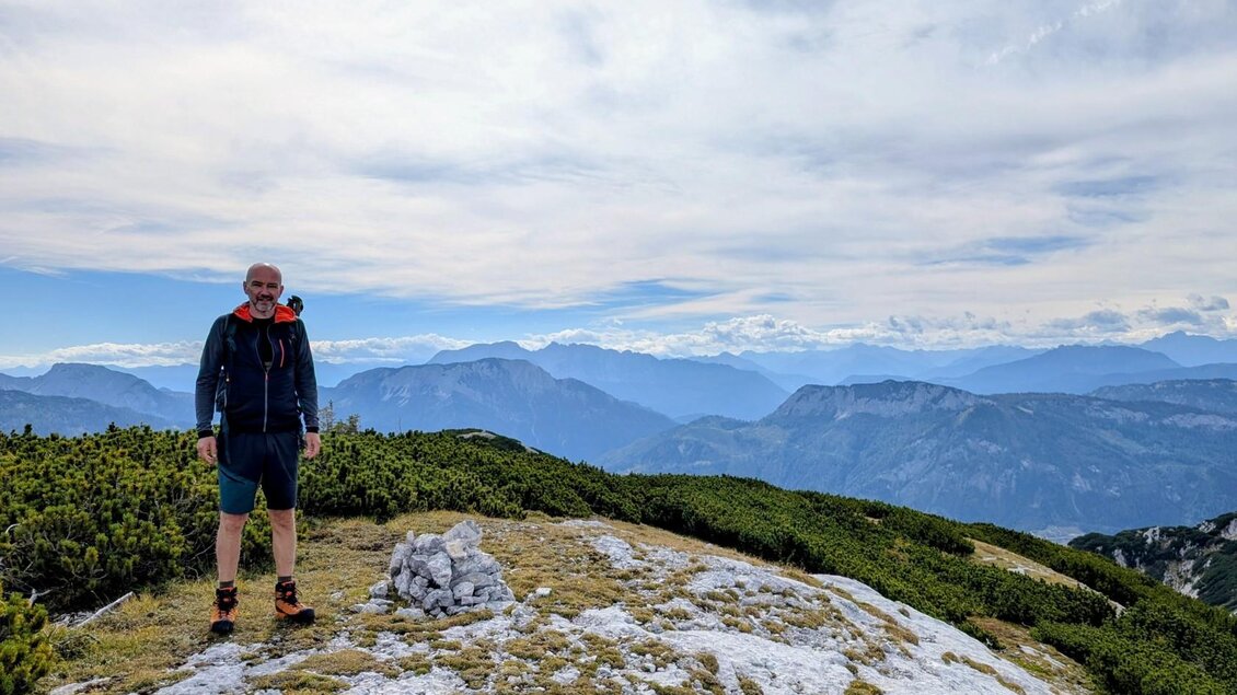 Der Bergführer steht auf einem Berg mit traumhaften Ausblick auf die beeindruckende Berglandschaft. Der Himmel ist teilweise bewölkt. | © Andreas Moser
