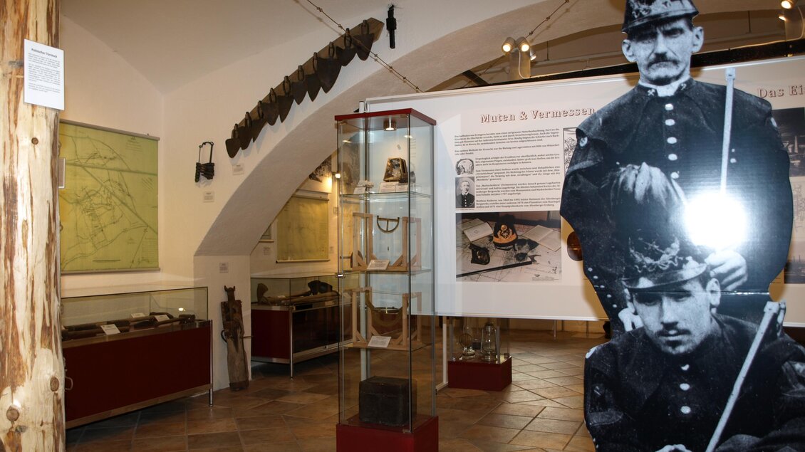 Ein Museum mit historischen Exponaten und einer Wandgrafik von Soldaten. Im Hintergrund sind Ausstellungsstücke in Vitrinen zu sehen. | © Erwin Gruber