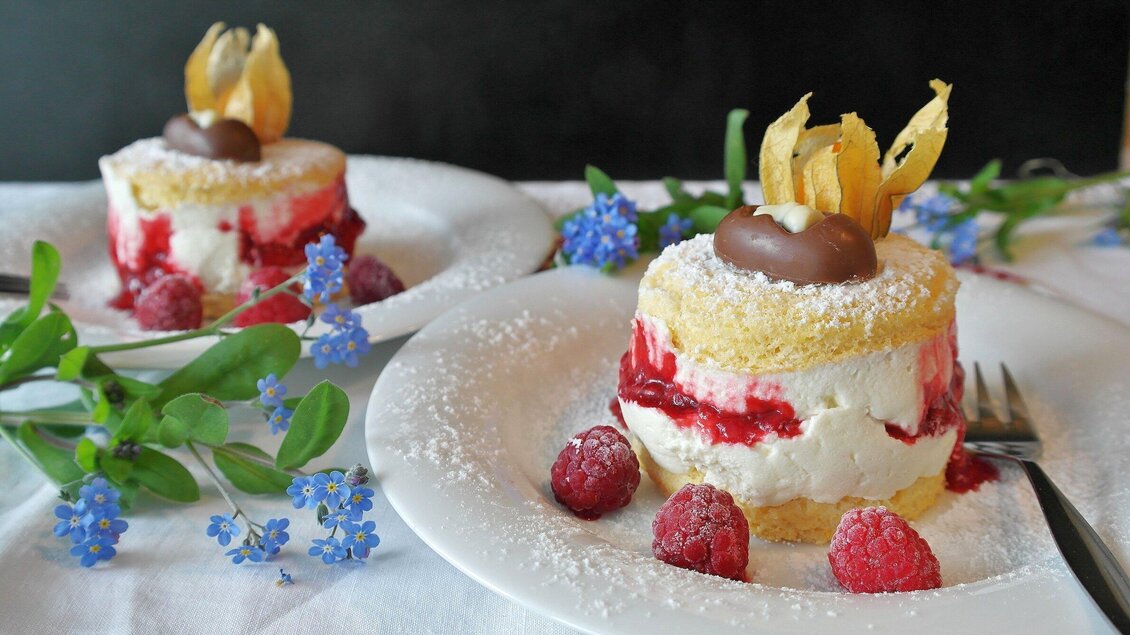 Zwei kleine Desserts mit Creme, Himbeeren und Schokolade, dekoriert mit essbaren Blüten beim Bergwirt Liebesnesterl in Köflach. | © Bergwirt