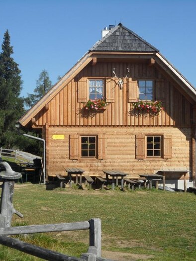 Holzhütte Bernsteinhütte in Hirschegg-Pack mit Blumenkästen, Sitzplätzen und Wanderweg in alpiner Landschaft. | © TV Lipizzanerheimat | EU