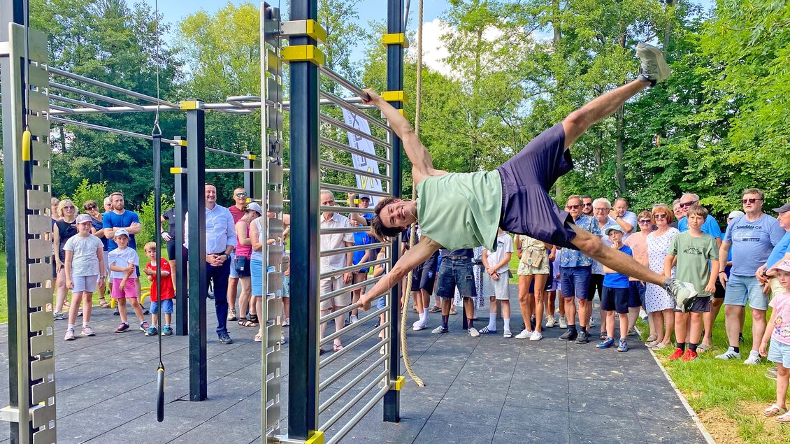 Ein Sportler demonstriert beeindruckende Kraft und Körperbeherrschung an den Geräten des Bewegungsparks in St. Stefan im Rosental, während zahlreiche Besucher:innen die Vorführung begeistert verfolgen. Der moderne Bewegungspark lädt Menschen jeden Alters zu Sport, Bewegung und gemeinsamer Aktivität im Freien ein. | © Marktgemeinde St. Stefan im Rosental