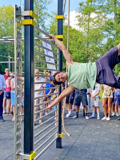 Ein Sportler demonstriert beeindruckende Kraft und Körperbeherrschung an den Geräten des Bewegungsparks in St. Stefan im Rosental, während zahlreiche Besucher:innen die Vorführung begeistert verfolgen. Der moderne Bewegungspark lädt Menschen jeden Alters zu Sport, Bewegung und gemeinsamer Aktivität im Freien ein. | © Marktgemeinde St. Stefan im Rosental